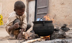 Au Niger, un jeune garçon est accroupi près d'un feu, en train de faire cuire des aliments dans une grande marmite.