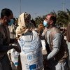 À Kandahar, en Afghanistan, Baryal Mumtaz et Feroz Aryan, membres du personnel de la FAO, aident un bénéficiaire à soulever un grand sac de semences de blé améliorées sur ses épaules.