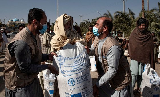 À Kandahar, en Afghanistan, Baryal Mumtaz et Feroz Aryan, membres du personnel de la FAO, aident un bénéficiaire à soulever un grand sac de semences de blé améliorées sur ses épaules.
