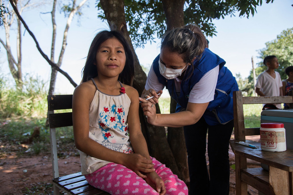 Una trabajadora sanitaria administra una vacuna a una niña en un entorno rural al aire libre en Paraguay.