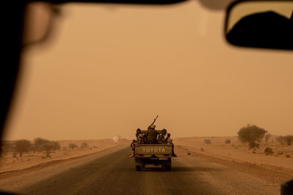 Vue depuis l'intérieur d'un pick-up Toyota transportant des militaires nigériens armés, circulant sur une route poussiéreuse dans la région d'Agadez, au Niger.