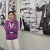 亚洲女子聂燕双臂交叉，站在艺术展览上，墙前展示着几幅大型马赛克肖像。
