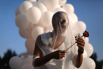 Una activista de la sociedad civil, vestida con un vestido blanco y velo, sostiene una rosa roja mientras celebra frente a un grupo de globos blancos.