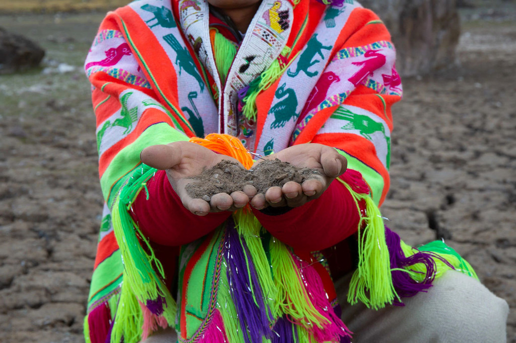 Hombre indígena con colorido atuendo tradicional sosteniendo tierra en sus manos.