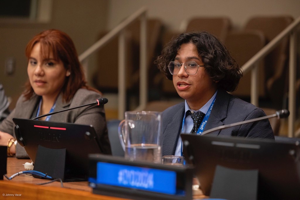 Rehman Hassan, a member of the WHO Youth Council, speaks at a formal meeting with a microphone and water pitcher on the table.