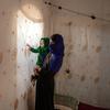An Afghan mother holds her daughter, staring at the light from behind her obscured window.