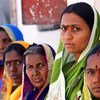 रंग-बिरंगी साड़ियों में लिपटी दक्षिण एशियाई महिलाओं का एक समूह कतार में खड़ा है और आगे की ओर देख रहा है।