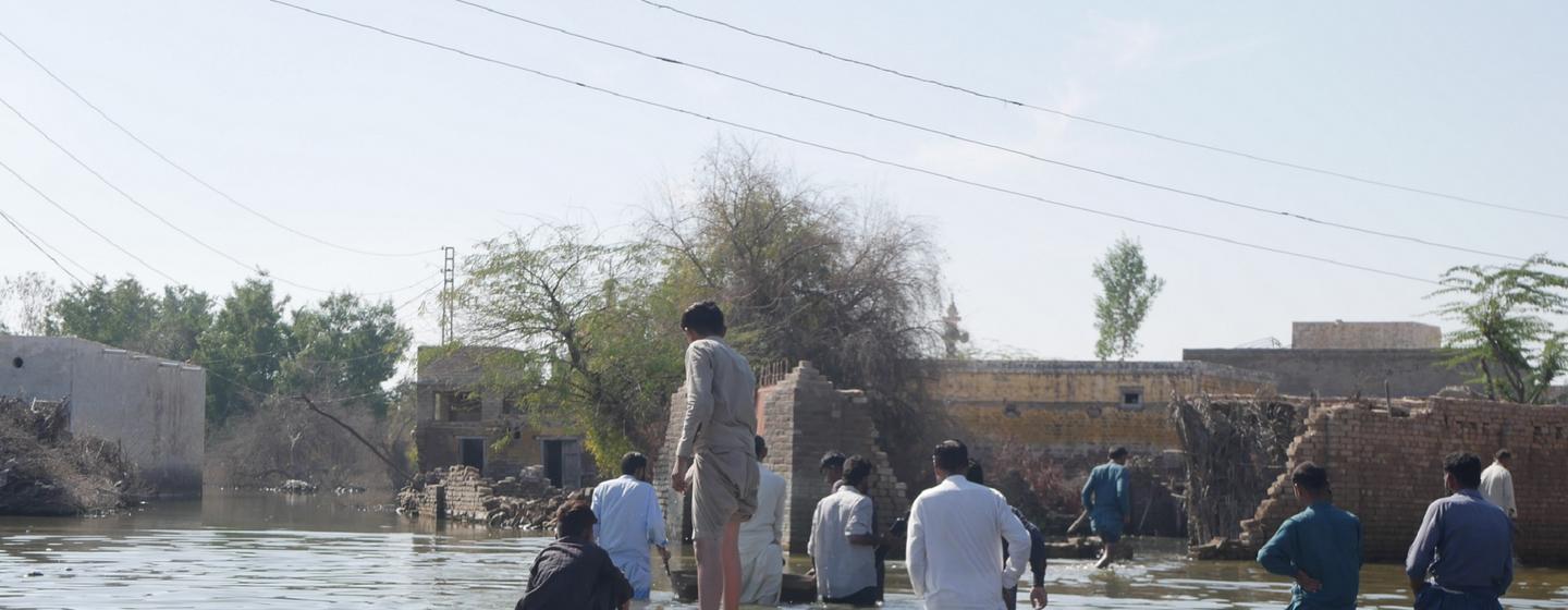 Des habitants se déplacent dans un village inondé au Pakistan, certains pataugeant dans l'eau tandis que d'autres utilisent un radeau de fortune.