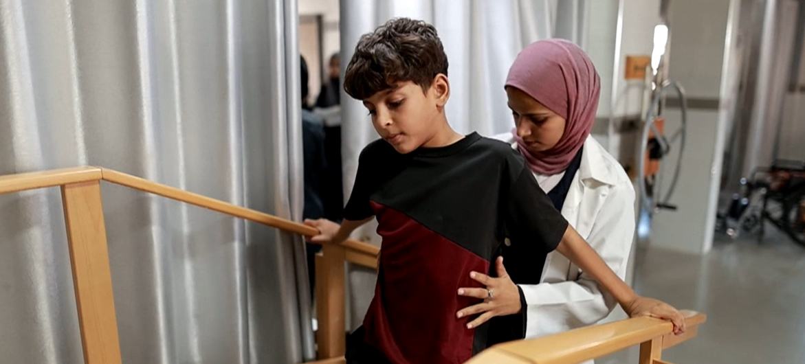 طفل فلسطيني يتلقى مساعدة في العلاج الطبيعي من أحد العاملين في مجال الرعاية الصحية في المستشفى.