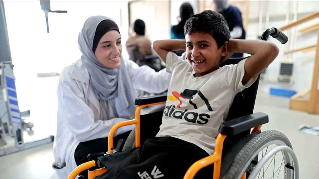 الطفل الفلسطيني أكرم، يتلقى رعاية إعادة التأهيل وإلى جواره الدكتورة فايزة برقان أخصائية العلاج الطبيعي في مستشفى الأمل، خان يونس - قطاع غزة