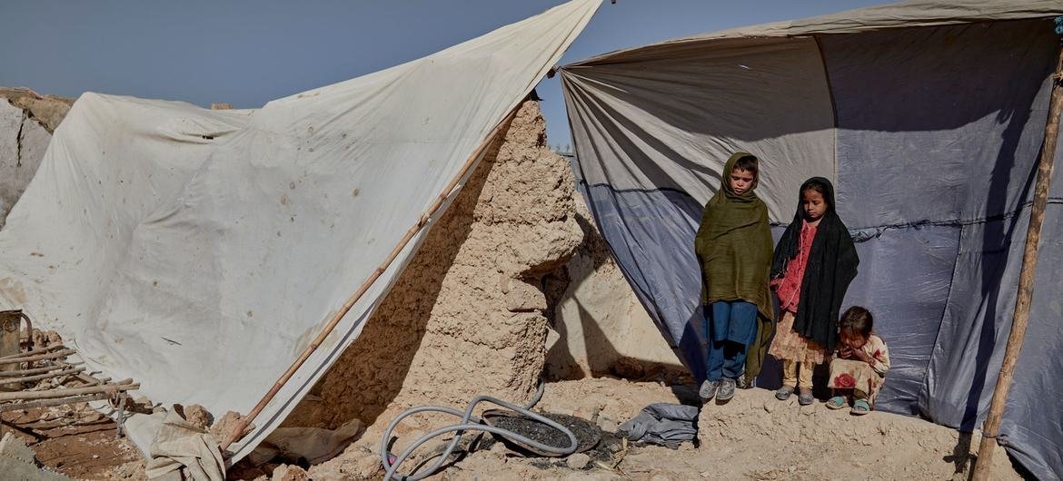 Three young Afghan children stand outside a damaged compound with makeshift tents in Lashkar Gah, Helmand Province.