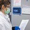Медицинский работник в лабораторном халате, маске и перчатках стоит перед ультранизкотемпературным морозильником в Базеле, Швейцария, проверяя температуру -69°C для хранения вакцины от Эболы.