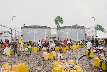 在刚果民主共和国戈马附近的一个流离失所者安置点，UNICEF工作人员和流离失所者用黄色塑料桶从大型金属水库中装水。