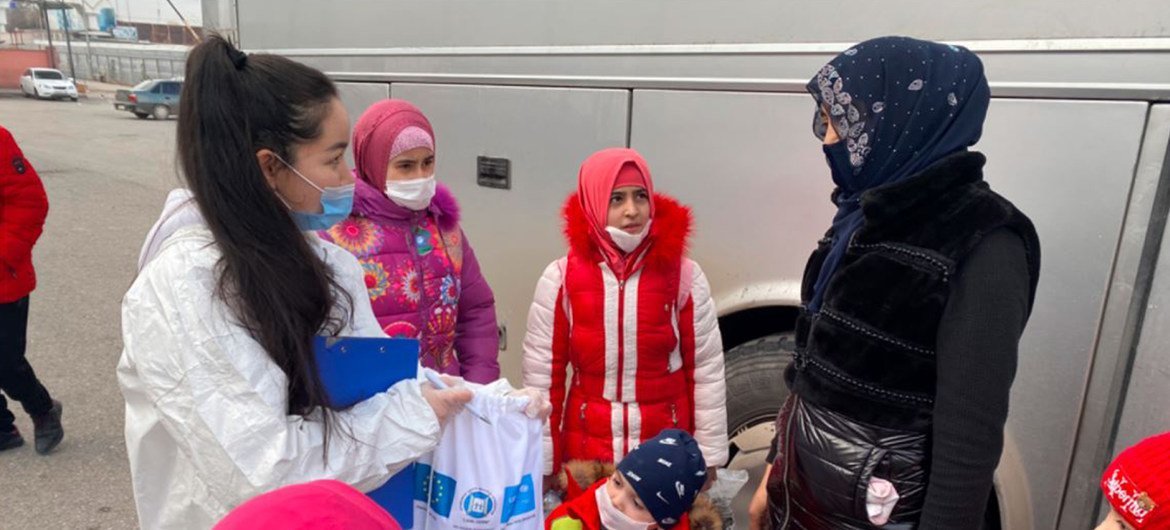 Uma funcionária da Unicef entrega uma sacola de doações a um grupo de mulheres e crianças, vestidas com roupas de inverno e em pé ao ar livre perto de um veículo grande.
