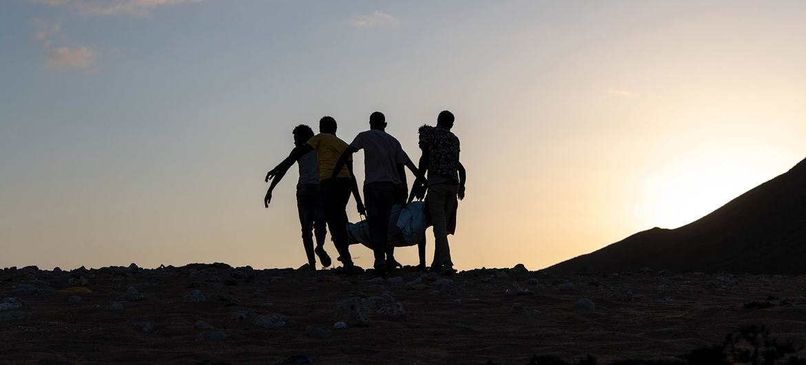 صور ظلية لأربعة رجال يحملون جثة في كيس عبر منظر صحراوي عند غروب الشمس في أوبوك، جيبوتي.