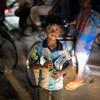 Um menino está em uma rua movimentada de Dhaka, Bangladesh, segurando uma flor e um pacote de objetos.