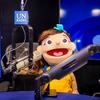 Una marioneta que representa a un personaje infantil está sentada en un estudio de radio con un micrófono de Radio ONU .