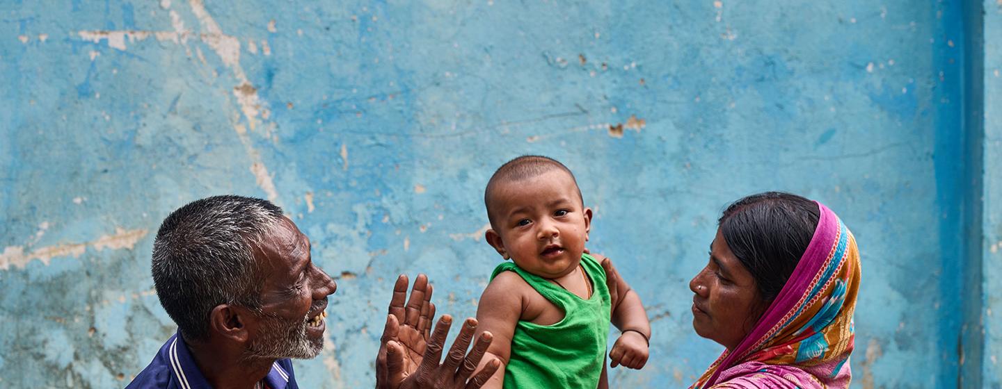 A baby is held by its mother and entertained by its grandfather at a community clinic in northern Bangladesh.