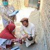 En Afghanistan, un père berce son enfant tandis que des agents de santé féminins administrent des vaccins contre la polio.
