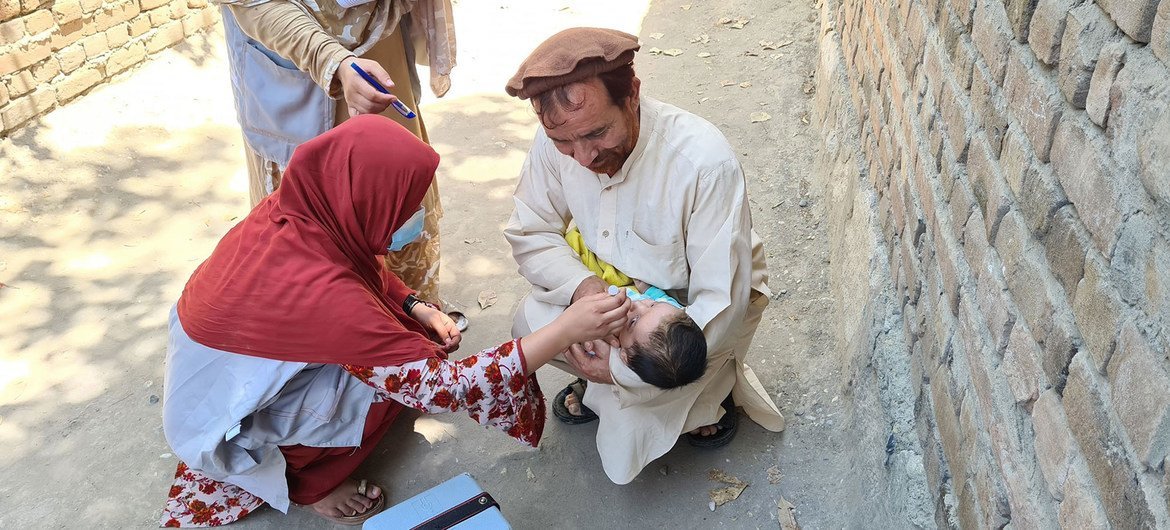 En Afghanistan, un père berce son enfant tandis que des agents de santé féminins administrent des vaccins contre la polio.