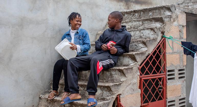 Uma jovem e um jovem sentam-se em uma escadaria de concreto em Maputo, Moçambique, sorrindo um para o outro.