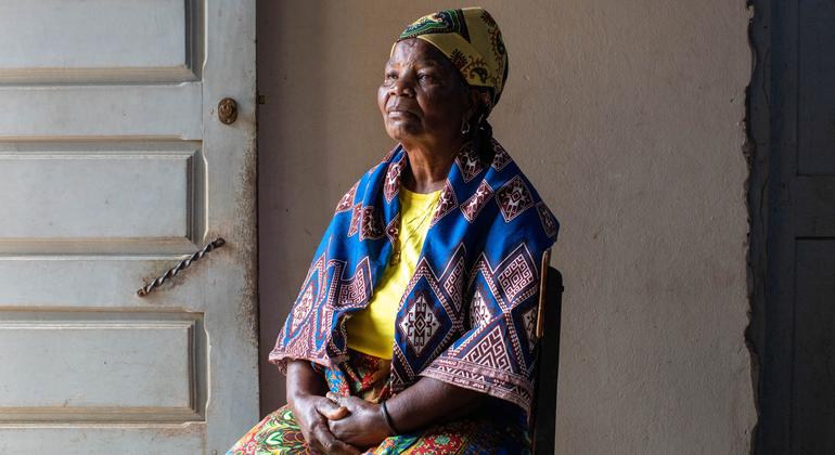 Uma senhora moçambicana idosa chamada Elisa está sentada em Maputo, vestindo trajes tradicionais, refletindo sobre a história democrática do país.
