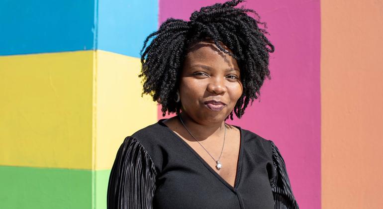 Retrato da voluntária do e-monitor+ Adelaide em Maputo, Moçambique, contra uma parede listrada colorida.