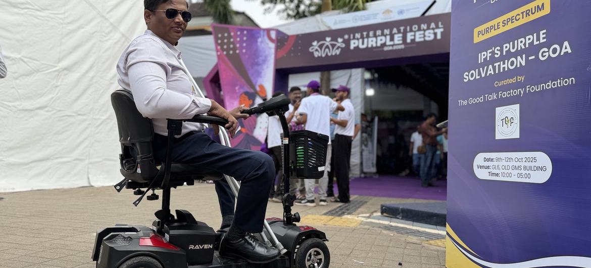 एक व्यक्ति मोबिलिटी स्कूटर पर बैठकर 2025 में गोवा में आयोजित होने वाले अंतर्राष्ट्रीय पर्पल फेस्ट के प्रवेश द्वार पर बैठा है, जो सुलभता का प्रदर्शन कर रहा है।
