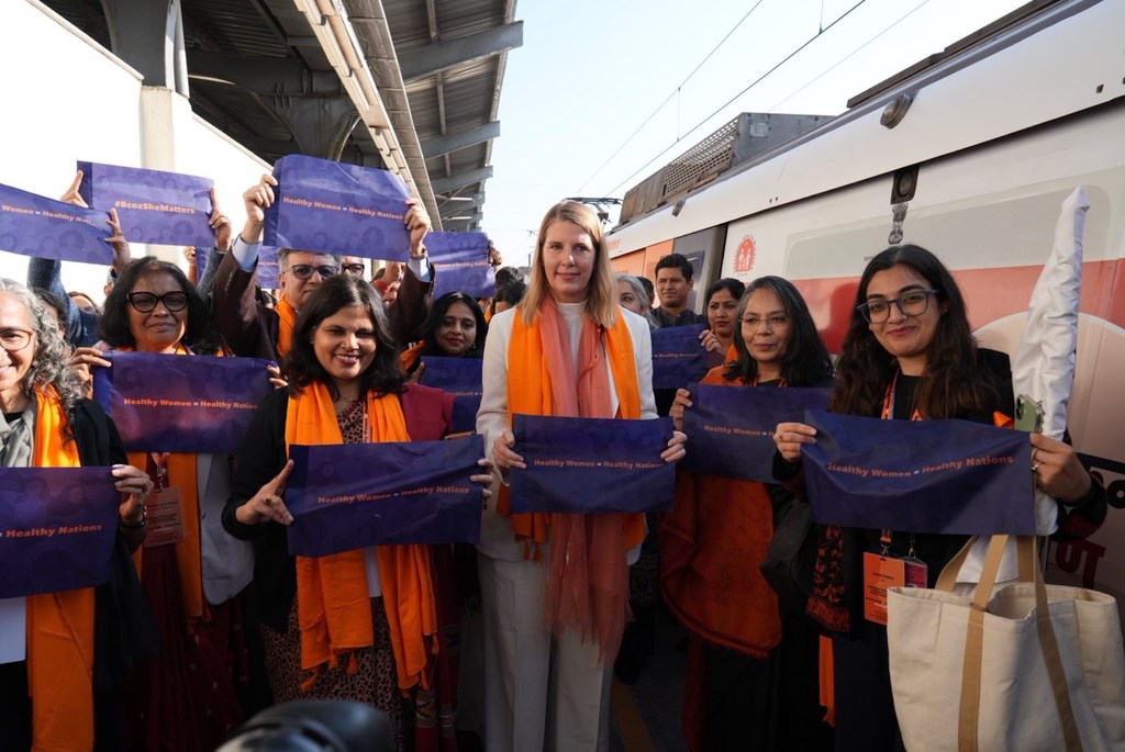 डब्ल्यूएचओ के अधिकारी और समर्थक महिलाओं के स्वास्थ्य पर केंद्रित एक जन स्वास्थ्य अभियान के लिए एक रेलवे स्टेशन पर नीले बैनर पकड़े हुए हैं।
