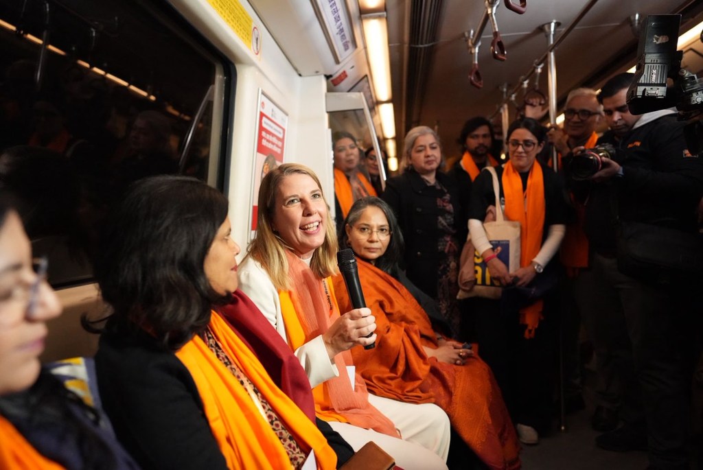 एक उद्घाटन अभियान यात्रा के दौरान मेट्रो ट्रेन में अधिकारी और आमंत्रित व्यक्ति मौजूद थे, जिनमें से एक महिला माइक्रोफोन में बोल रही थी।