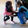 À l'aéroport de Lisbonne, un membre du personnel du HCR , vêtu d'un gilet bleu, s'accroupit pour saluer un jeune enfant et un tout-petit.