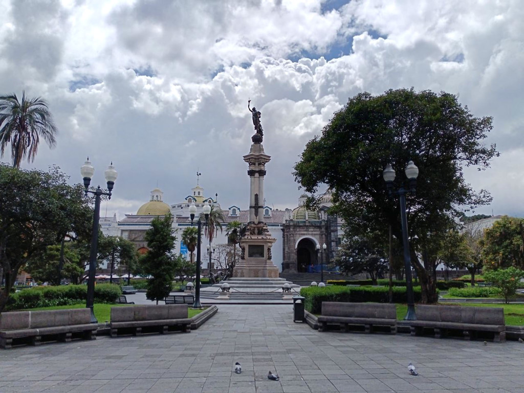 Una plaza vacía en Quito, Ecuador, con un monumento central y edificios de estilo colonial bajo un cielo nublado.