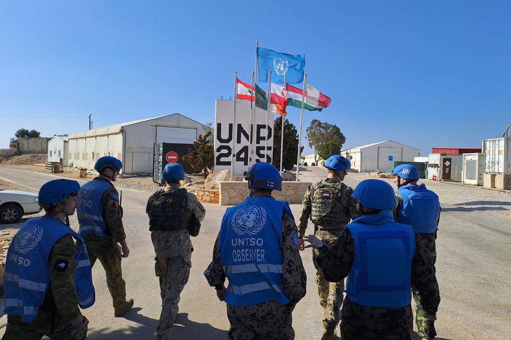 مراقبون عسكريون UNTSO يرتدون الخوذات والسترات الزرقاء يقفون بالقرب من لافتة برنامج الأمم المتحدة الإنمائي رقم 245 مع الأعلام، يراقبون عمليات حفظ السلام في الشرق الأوسط.