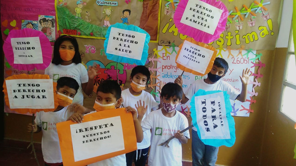 Des enfants tenant des pancartes avec un texte en espagnol sur leurs droits, notamment « J'ai le droit à une famille » et « Respectez nos droits », dans un cadre scolaire.