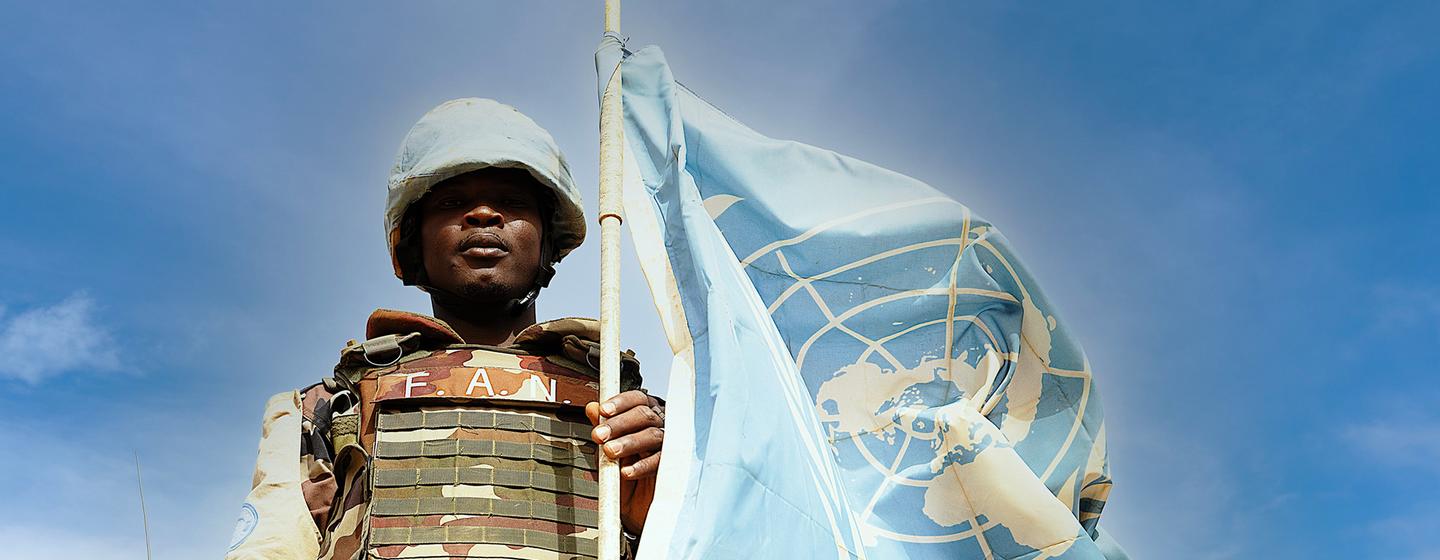 Un Casque bleu nigérien pose devant le drapeau des Nations Unies à Ménaka, dans le sud-est du Mali.