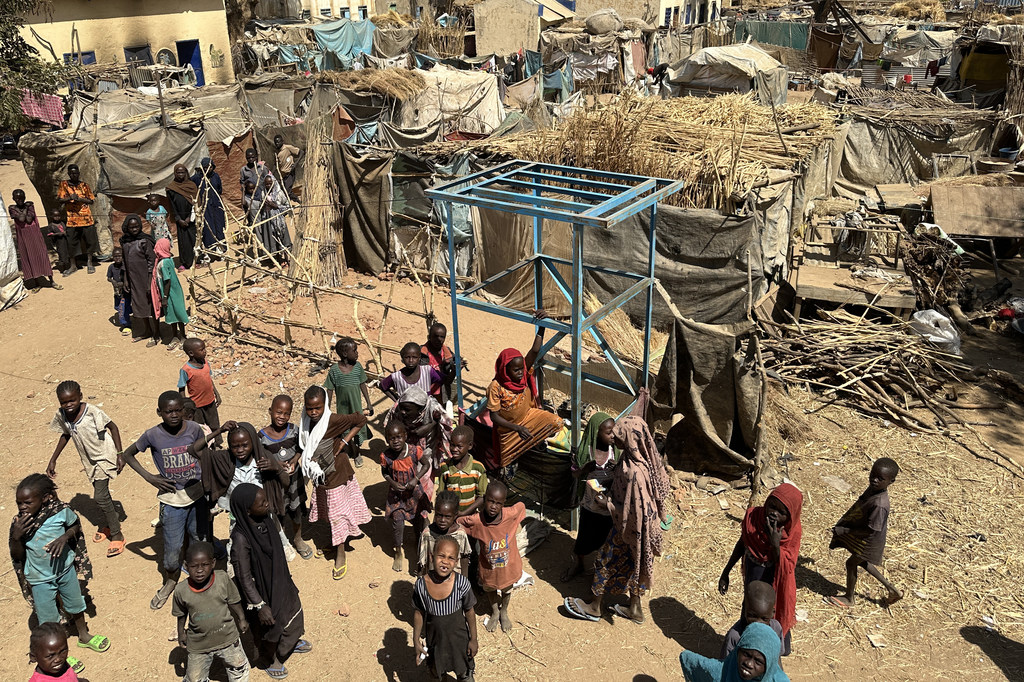 Vue aérienne d'enfants et de leurs familles debout près des abris temporaires du site de Khamsa Dagiga pour personnes déplacées dans la ville de Zelingei, Darfour central, au Soudan