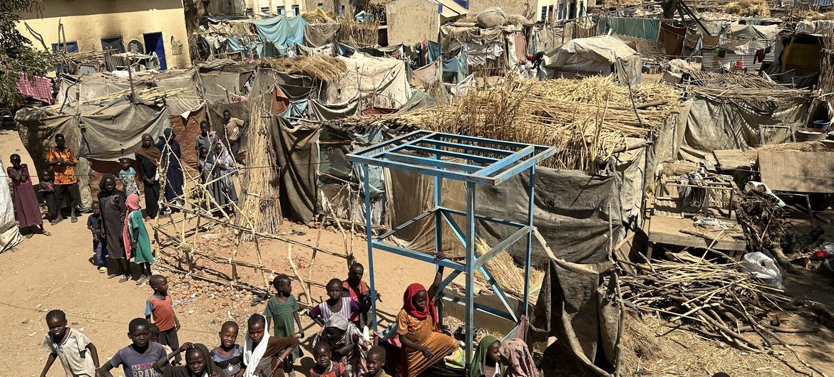 An aerial view of children and their families standing near temporary shelters at the Khamsa Dagiga site for displaced people in Zelingei Town, Central Darfur, Sudan
