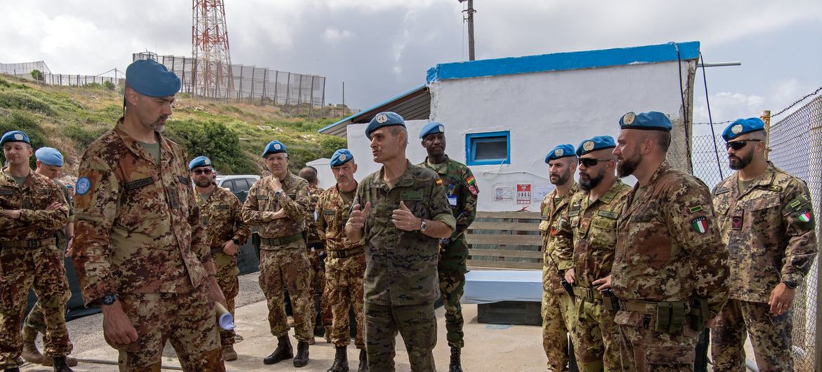 Un grupo de cascos azules de la UNIFIL , vestidos con uniformes de camuflaje y boinas azules, se reúne al aire libre en una base militar para una sesión informativa.