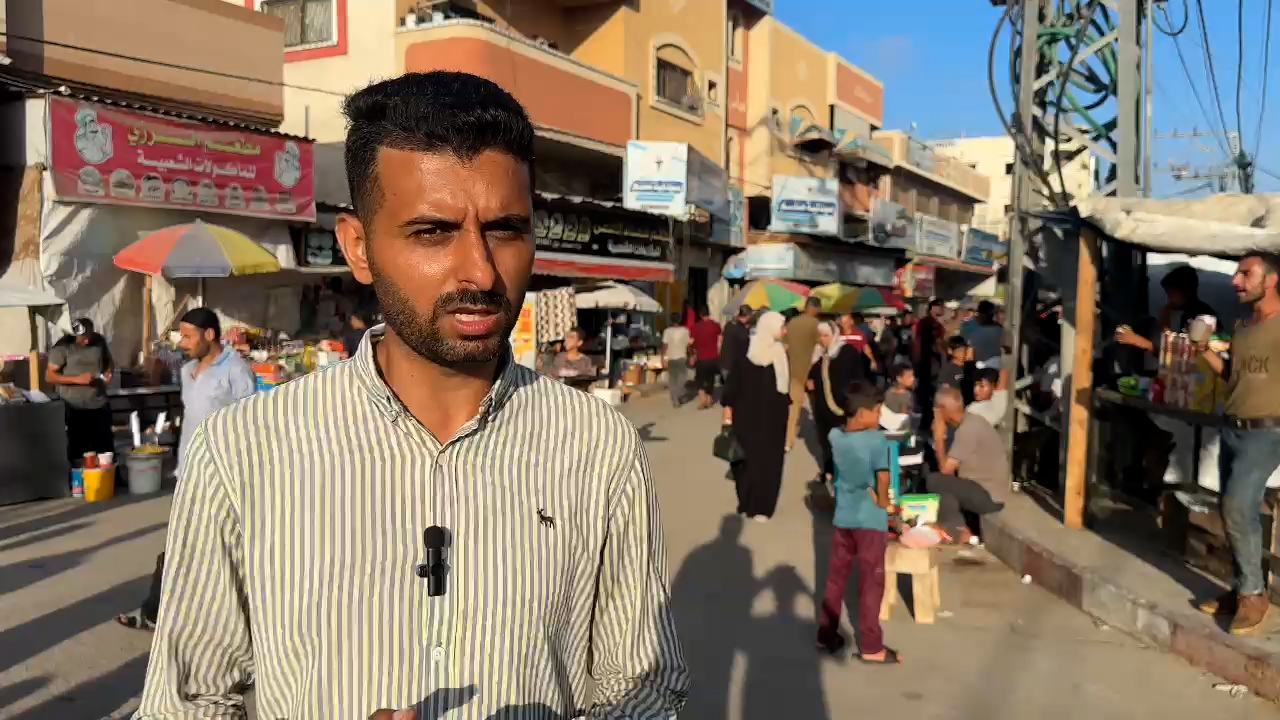 Mohamed Jarbou, an internally displaced Palestinian in Deir Al-Balah, Gaza Strip, speaks into a microphone on a busy street market.