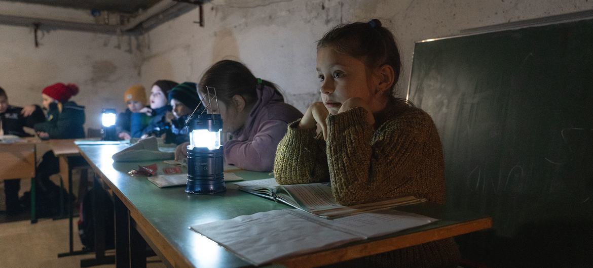 Children in Borodianka, Ukraine, study under lamplight in a shelter.
