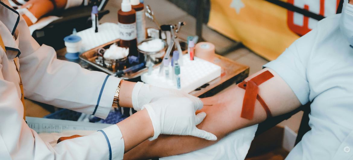 A medical professional in white gloves draws blood from a donor's arm.