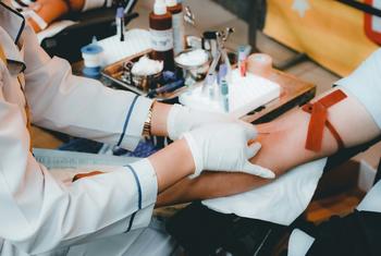 A medical professional in white gloves draws blood from a donor's arm.