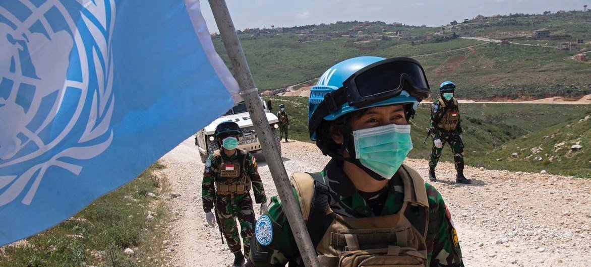 Soldados de paz da Unifil , vindos da Indonésia e usando máscaras, patrulham a Linha Azul no sul do Líbano. Um dos soldados carrega uma grande bandeira da ONU .