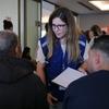 Funcionário da OIM vestindo um colete azul conversa sobre documentos com dois homens em um centro comunitário em Brasília, Brasil.
