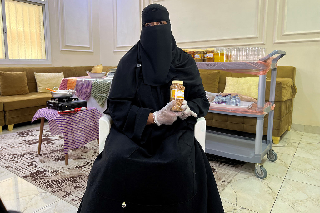 نورة خالد مصيفر تحمل جرة من التوابل وهي ترتدي النقاب والقفازات، جالسة في غرفة بها عربة لتحضير الطعام.