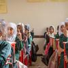 Estudantes jovens, mulheres de uniforme verde e hijab branco, levantam as mãos em uma sala de aula da Escola Omar bin Al-Aas, em Al-Wadi, Marib, Iêmen.