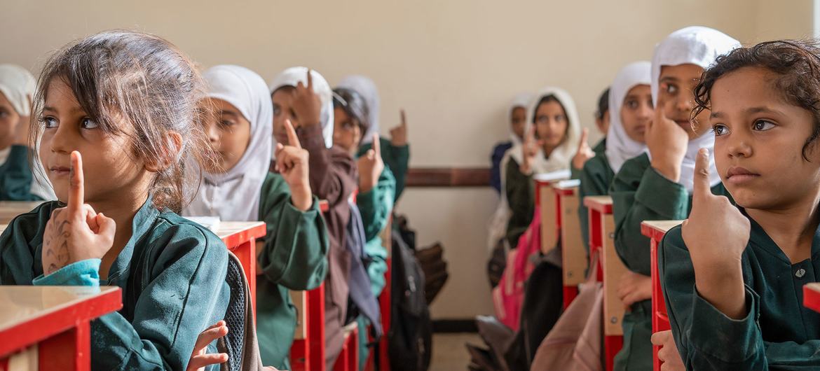 Estudantes jovens, mulheres de uniforme verde e hijab branco, levantam as mãos em uma sala de aula da Escola Omar bin Al-Aas, em Al-Wadi, Marib, Iêmen.