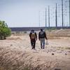 两名男子走在分隔墨西哥和美国的边境墙旁边。