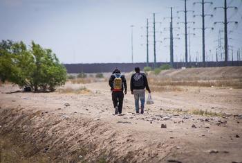 Dos hombres caminan junto al muro fronterizo que divide México de Estados Unidos.