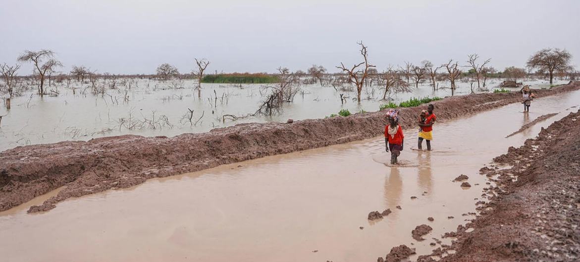 People displaced by flooding carry children and belongings along a waterlogged road in Bentui, South Sudan. (file)